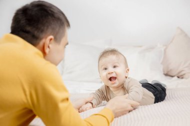 Genç baba yeni doğmuş bebekle yatakta oynuyor.