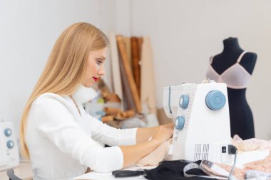 Beyaz kadın terzi dikiş makinesinde çalışıyor.