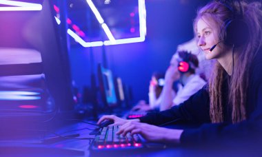 Flamalı genç kadın, kulaklıklı, neon renkli bilgisayar oyunu oynayan profesyonel oyuncunun zaferine seviniyor