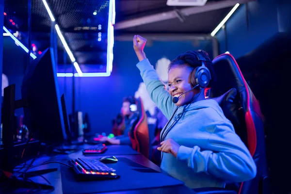 Streamer Africano jovem mulher se alegra na vitória jogador profissional jogar jogos online computador com fones de ouvido, cor néon — Fotografia de Stock