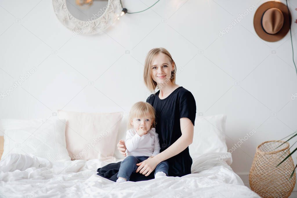 Happy family, girl child sitting young mother on knees in bedroom. Bright Scandinavian interior
