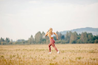 Atletik genç sarışın kız parkın şafağında koşuyor, sağlık koşusu konsepti.