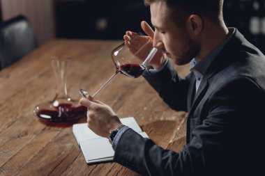 Sommelier restoran için alkol tatma kartı hazırlıyor, bardaktaki kırmızı şarabı değerlendiriyor.