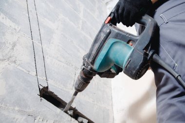 İnşaat işçisi havalandırma boruları için inşaat duvarını delmek için matkap kullanıyor.