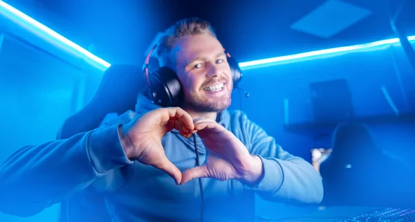 Streamer hermoso hombre muestra el signo del corazón con manos jugador profesional jugando juegos en línea ordenador, color neón — Foto de Stock