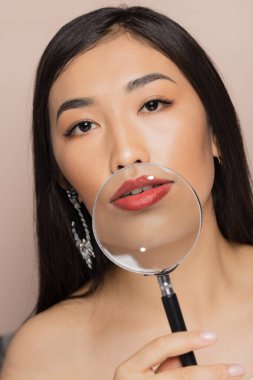 Dudak büyütme kavramı doğaldır. Moda genç Asyalı kadın arka planda büyüteç tutuyor.