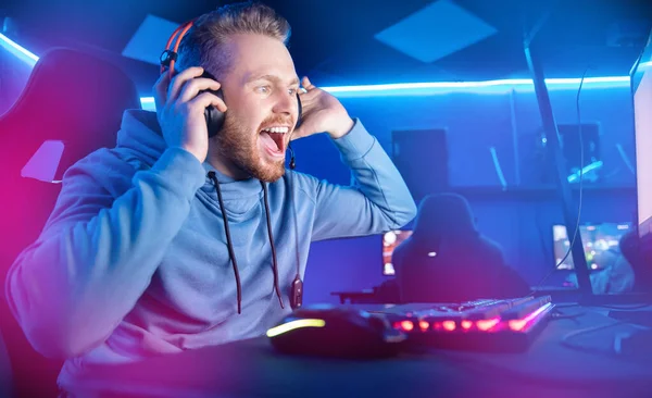 Streamer fiatal férfi örül a győzelemben profi játékos játék online játékok számítógép fejhallgató, neon szín — Stock Fotó