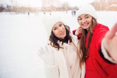 Arkadaşlık yaşam tarzını kabul et. Mutlu gülümseyen çift kadın buz pateni pistinde akıllı telefonuyla fotoğraf çekiyor.
