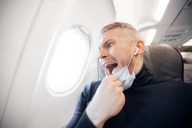 Kuş fobisi ya da kuş fobisi kavramı. Uçakta ve uzun boylu, sağlık maskeli bir turistten korkuyorlar.