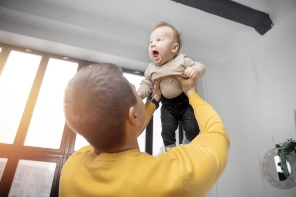 Lycklig far leker med lille son hemma på bakgrund av fönster, spyr, pojke skrattar och ler — Stockfoto