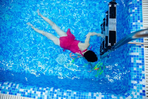 Private swimming lesson, woman coach is teaching child girl in pool, top view