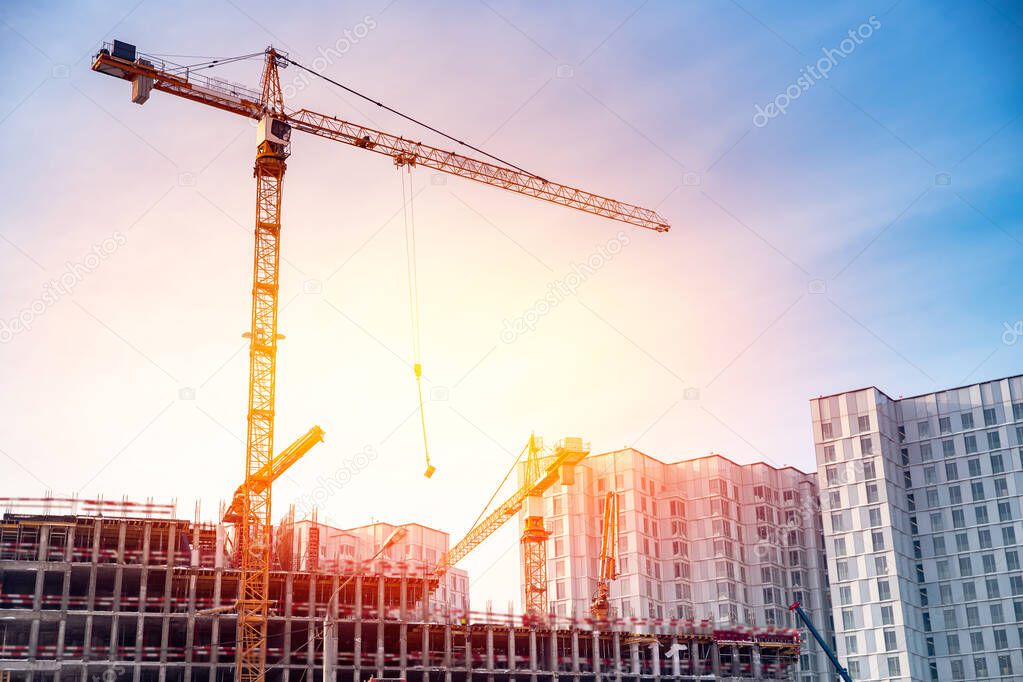 Sunset construction site of modern apartment buildings with steel structures and cranes against blue sky