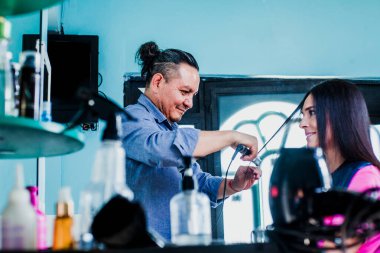 Latin bir adam kuaförlük yapıyor ve Mexico City 'de küçük bir güzellik salonunda kadın bir müşterinin saçını kesiyor.