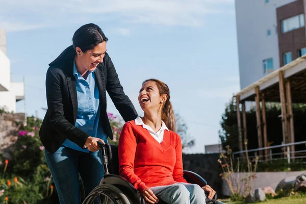 Happy young latin woman in wheelchair and her friend having fun outdoors in Mexico