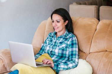 Latin kadın kanepede oturuyor ve Meksika 'da dizüstü bilgisayarla çalışıyor.