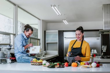 Meksikalı çift Meksika mutfağında Meksika yemeği pişirirken yemek tarifleriyle kitap okuyor.