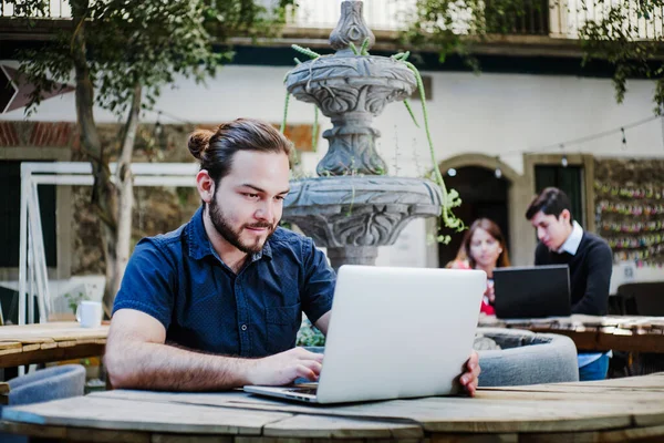 Young latin college man using computer while sitting in the college yard