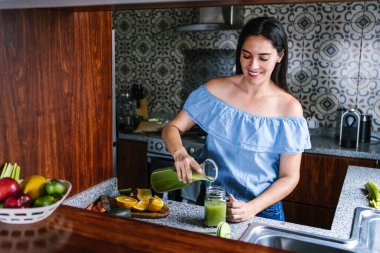 Latin Kadın Meksika 'da sağlıklı beslenme kavramında mutfakta yeşil smoothie veya detoks suyu yapıyor.