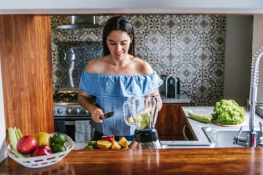 Latin Kadın Meksika 'da sağlıklı beslenme kavramında mutfakta yeşil smoothie veya detoks suyu yapıyor.