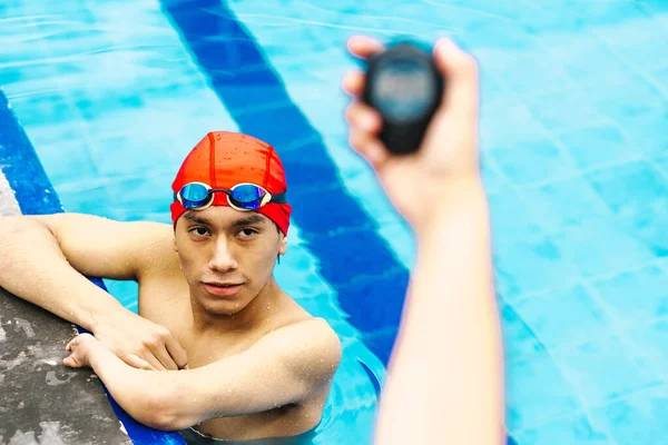 hand holding a timer chronometer with a young man in the background at the swimming pool in Mexico Latin America