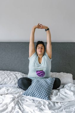 Ayrıca Latin Amerika 'da yatakta oturan ve kollarını geren boyunda bir Latin kadın..