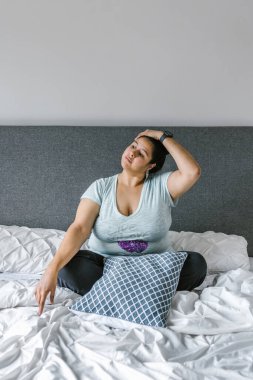 Latin kız artı boynu rahatlatan boynu Latin Amerika 'da yatakta oturan, artı beden ölçülerinde bir kadın.