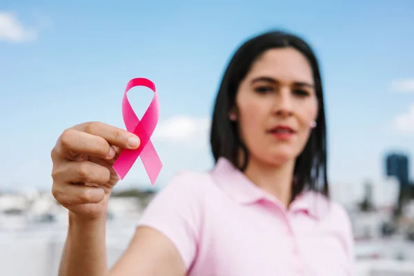 portrait of latin woman hand holding pink breast cancer awareness ribbons with blue sky as background in Latin America