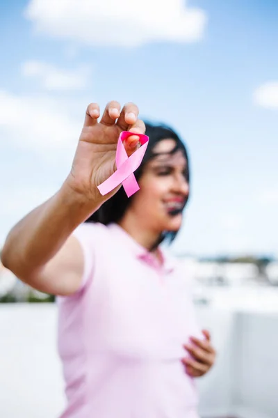 portrait of latin woman hand holding pink breast cancer awareness ribbons with blue sky as background in Latin America