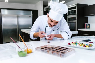 Latin Amerika 'da ticari bir mutfakta, Meksika çikolatası tabağında duran şef şapkalı genç Latin adam.