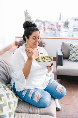 Latin Amerika 'da terasta oturan kıvrımlı Meksikalı kadın salata yiyor.