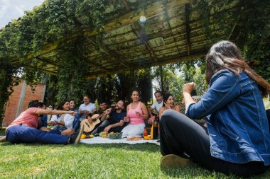 Latin kökenli büyük bir aile, Meksika Latin Amerika 'da güneşli bir hafta sonu gününde parkta piknik örtüsünde oturuyor. Hispanik çeşitliliği ve çok nesilli insanlar açık hava faaliyetlerinde