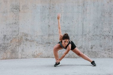 Şehirdeki kentsel alanda spor kıyafetleri içinde esneyen ve egzersiz yapan genç İspanyol kadın.