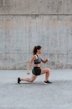 Şehirdeki kentsel alanda spor kıyafetleri içinde esneyen ve egzersiz yapan genç İspanyol kadın.