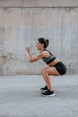 Şehirdeki kentsel alanda spor kıyafetleri içinde esneyen ve egzersiz yapan genç İspanyol kadın.