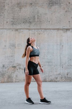 Şehirdeki kentsel alanda spor kıyafetleri içinde esneyen ve egzersiz yapan genç İspanyol kadın.