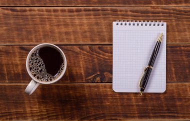 Bir fincan kahve ve eski ahşap masa arka planında kalem olan not defteri..