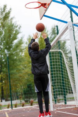Sevimli genç çocuk sokak parkında basketbol oynuyor. Dışarıda turuncu basketbol topu olan bir genç. Hobi, aktif yaşam tarzı, çocuklar için spor aktivitesi.