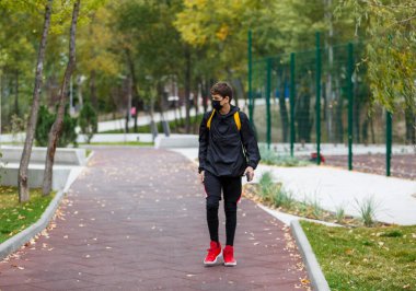 Yüzünde siyah koruyucu maske olan yakışıklı bir çocuk. Korona virüsünden, hastalıktan, enfeksiyondan korunmak için tıbbi maske takan bir genç. Şehir sokaklarında karantina