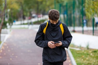 Yüzünde siyah koruyucu maske olan yakışıklı bir çocuk. Korona virüsünden, hastalıktan, enfeksiyondan korunmak için tıbbi maske takan bir genç. Şehir sokaklarında karantina