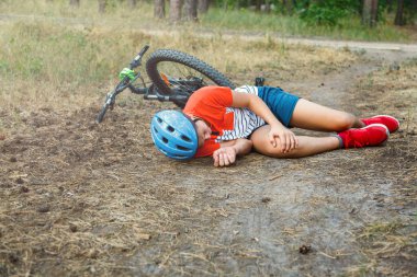 Kasklı beyaz bir çocuk kaza geçirdi ve bisikletten düştükten sonra yere oturdu. Yazın ormanda dizinde ağrı hissetti. Güvenlik kavramı, bisiklet kazası.