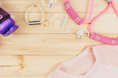 Ahşap arka plandaki kadınlar için spor kıyafetleri ve aksesuarlar. Tişörtlü spor modası, elastik bantlar, kulaklıklar, spor ayakkabıları, şişe. Sağlıklı, aktif yaşam tarzı konsepti