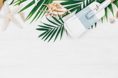 Tropik palmiye yaprakları, hasır şapka, denizyıldızı, beyaz ahşap arka planda deniz kabukları. Moda tropikal desen. Moda kıyafetleri ve aksesuarlar. Düz yat, kapat. Yaz, tatil, tatil konsepti.