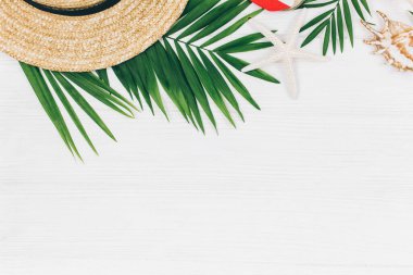 Tropik palmiye yaprakları, hasır şapka, denizyıldızı, beyaz ahşap arka planda deniz kabukları. Moda tropikal desen. Moda kıyafetleri ve aksesuarlar. Düz yat, kapat. Yaz, tatil, tatil konsepti.