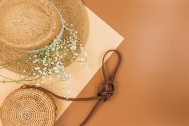 Tropik hasır şapka, çanta, bej kahverengi arka planda yaz çiçekleri. Moda tropikal desen. Moda kıyafetleri ve aksesuarlar. Düz yat, kapat. Yaz, tatil, tatil konsepti.