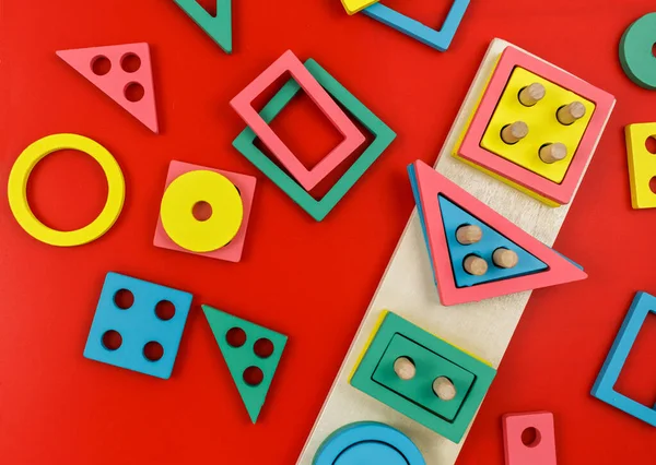 Multicolored wooden blocks on red background. Trendy puzzle toys. Geometric shapes: square, circle, triangle, rectangle. Educational toys for kindergarten, preschool or daycare. Back to school