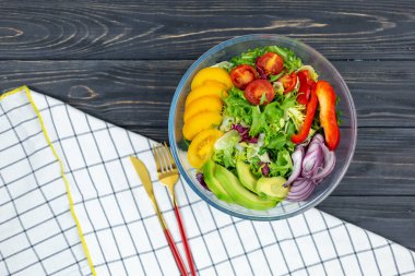 Taze yeşil salata, avokado, domates, biber, ahşap tepside büyük beyaz kasede soğan. Yeşil yapraklı ve sebzeli vejetaryen salatası. Gri masadaki üst manzara. Sağlıklı vejetaryen yemekleri. Kapat.