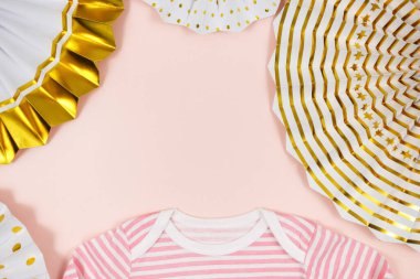 Pembe tulum, kağıt yelpaze ve pembe masadaki yeni doğmuş kız için aksesuarlar. Organik pamuktan bebek tulumu maketi. Bebek partisi, festival, doğum günü partisi dekorasyonu.