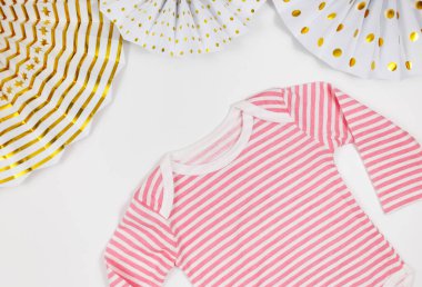 Pembe tulum, kağıt yelpaze ve beyaz masadaki yeni doğan kız için aksesuarlar. Organik pamuktan bebek tulumu maketi. Bebek partisi, festival, doğum günü partisi dekorasyonu.