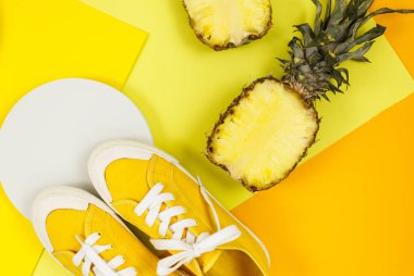 Ürünleri göstermek için ananas, spor ayakkabısı ve podyumları olan son moda parlak sarı arka plan. Yaz, tatiller, yemek konsepti. Düz yat, üst görünüm, maket yap..