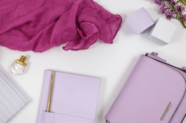 Beyaz arka planda mor deri kadın çantası, planlayıcı, eşarp, parfüm ve geometrik şekiller. Üst manzara, düz yatış. Moda kadın aksesuarları..